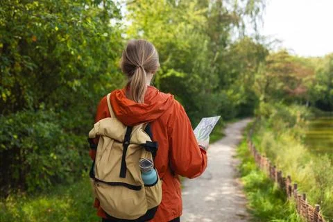Back view of young woman with backpack walking on forest path holding map Stock Photos