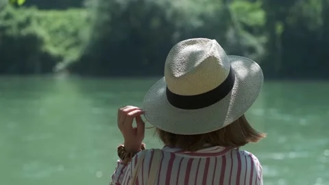 Back view of a young woman with a hat standing near the fast-flowing riverin 4k. Stock Footage 156902004