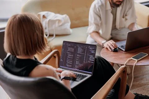Back view of young woman programmer writes program code on laptop while sitting Stock Photos