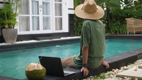 Back view of young woman using laptop at poolside Stock Footage 250261932