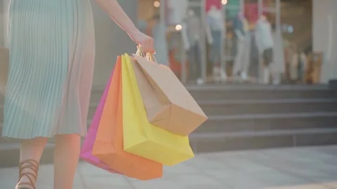 Back view of young woman's legs and colorful shopping paper bags Stock Footage 155944021