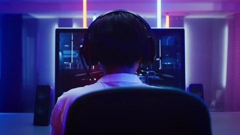 Back View Zoom Out Shot of the Professional Gamer Playing in Online Shooter. Vidéo 92411575