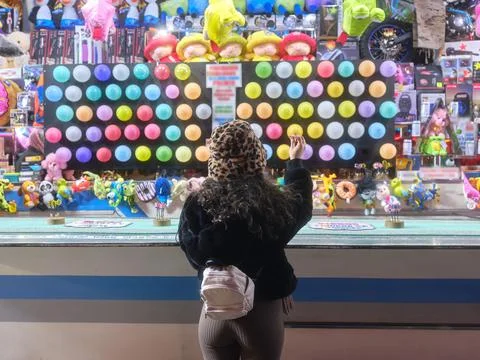 Back of a woman standing while throwing a dart at a night-time fair Stock Photos