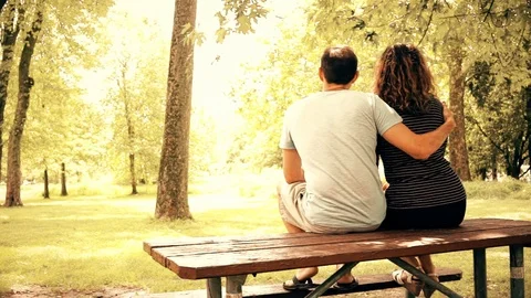 Back of young couple sitting on picnic table in outdoor park hugging, embracing Stock Footage 80207954
