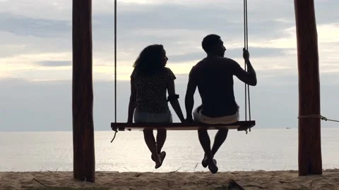 Back of young couple sitting on the swing at the beach talking and relaxing. Stock Footage 148973580