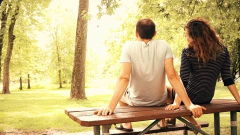 Back of young couple sitting on top of picnic table in outdoor park sunbathing Stock Footage 80208026