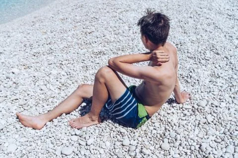 Back of a young man sitting on a stone beach Stock Photos