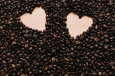Background with array of dry coffee beans with two heart shapes. Beige Stock Photos