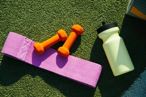 On the background of artificial grass there is a mat, a bottle, a fitness ela Stock Photos