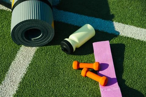 On the background of artificial grass there is a mat, a bottle, a fitness ela Stock Photos