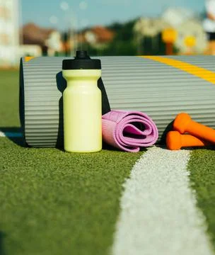 On the background of artificial grass there is a mat, a bottle, a fitness ela Stock Photos