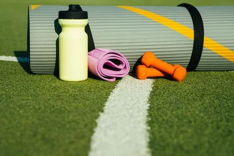 On the background of artificial grass there is a mat, a bottle, a fitness ela Stock Photos