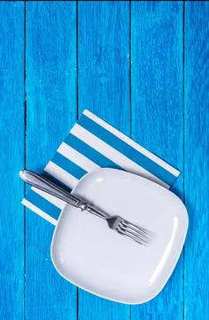 Background with empty squared white ceramic plate and silver fork on blue wooden Stock Photos