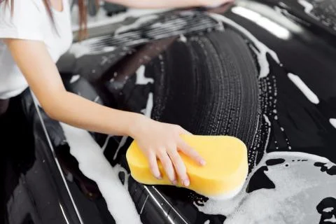 Background hand hold sponge over black car for washing white foam. Top view Stock Photos
