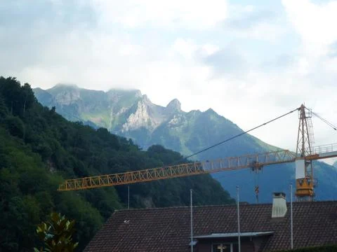 On the background of mountains, a construction tower crane above the roof Stock Photos