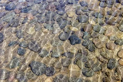Background of small stones lying under water. Stones in the water. Stock Photos