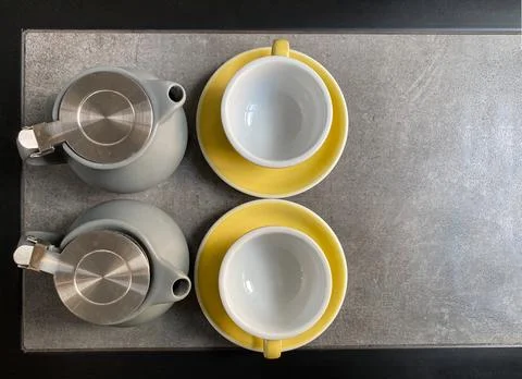 Background of two gray tea kettles and two yellow mugs standing on the table Stock Photos