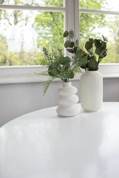 Background of two white vases with artificial greenery on white table and w.. Foto stock