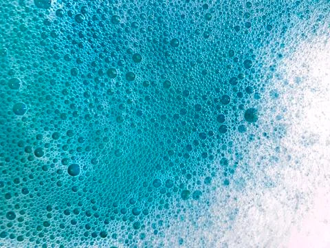Background with white soap foam in blue turquoise bright water. Ocean or bath Stock Photos