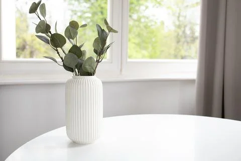 Background of white vase with artificial eucalyptus on white table and wind.. Stock Photos