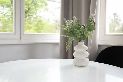 Background of white vase with artificial greenery on white table and window.. Foto stock