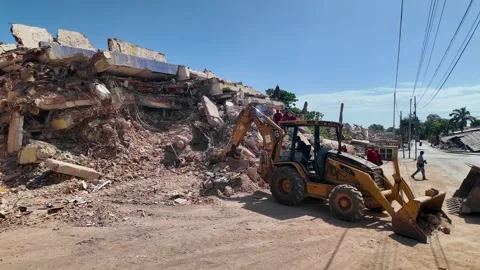 Backhoe excavator clearing heavy concrete rubble and debris at earthquake Stock Footage 341434199