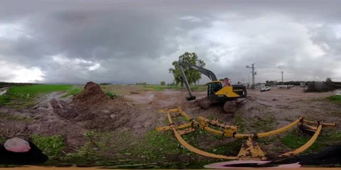 A backhoe loader clears twigs for draining a clogged stream during rain 360VR 스톡 동영상 145292020