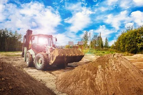 Backhoe loader collects sandy material from high pile, transporting loose e.. Stock Photos