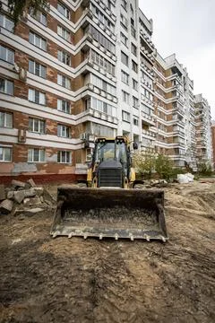 A backhoe loader is on a construction site in front of a tall apartment build Fotos de archivo