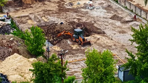 Backhoe loader digging a pit at a building construction site on a summer day Stock Footage 337388049