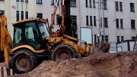 Backhoe loader digging soil at urban construction site near buildings Stock Footage 332130865