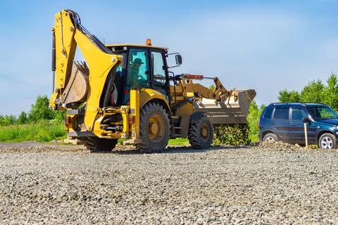 Backhoe loader dumping gravel from front bucket for site preparation under clear Stock Photos