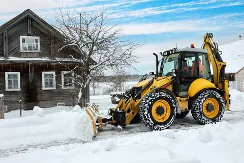 Backhoe loader with hydraulic front-mounted snow blade clears compacted sno.. Stock Photos