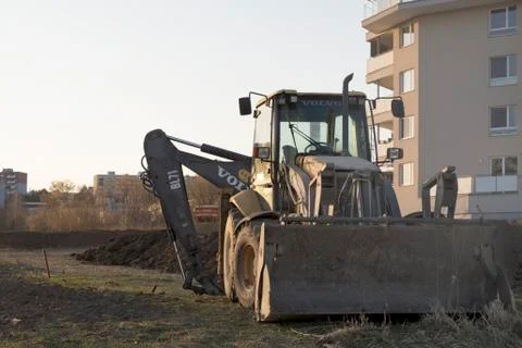 Backhoe loader infront of block of completed flats. Digger parked in sunset l Stock Photos