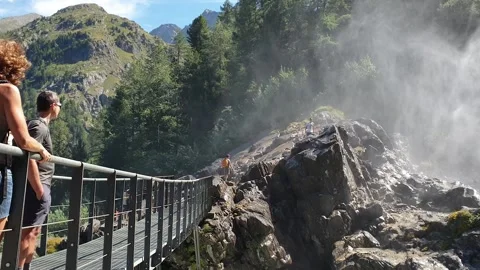 Backlight alpine waterfalls with a bridge over it and trekkers Stock Footage 137394486