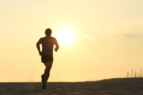 Backlight of a jogger running on the beach Stock Photos