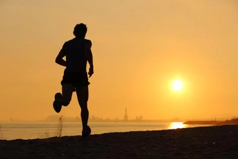 Backlight of a man running on the beach at sunset Stock Photos