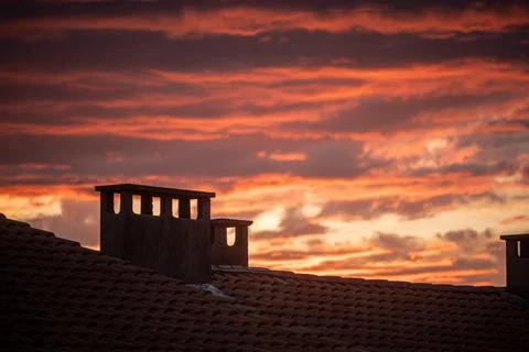 Backlit building rooftops against a cloudy sunset Stock Photos