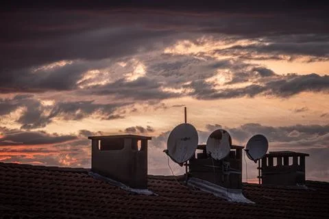 Backlit building rooftops against a cloudy sunset Stock Photos