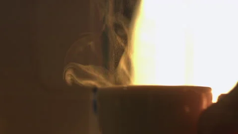 Backlit close up: Mug of steaming hot coffee is picked up by left hand Stock-Footage 197806544