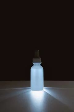 Backlit face serum in matte bottle on dark background Stock Photos