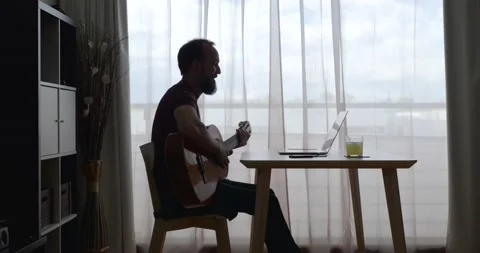 Backlit middle-aged man at home receiving guitar lessons via conference call Stock Footage 154636629