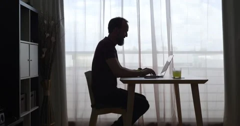 Backlit middle-aged man working with his laptop at home seated at a table nex Stock Footage 154636523