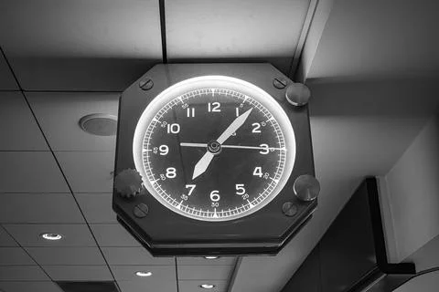 A backlit octagonal analog clock with a dark face and glowing numerals is Stock Photos