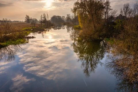 A backlit photo of tree and cloud reflections in a river. Beautiful sunset sky Stock Photos