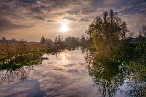 A backlit photo of tree and cloud reflections in a river. Beautiful sunset sky Stock Photos