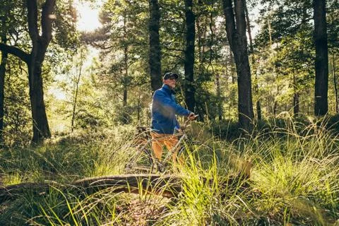 Backlit retired man standing in forest with bicycle. Stock Photos