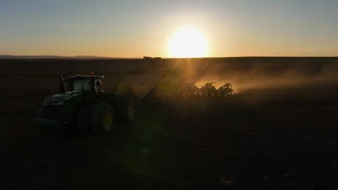 Backlit by setting sun, agriculture tractor seeds wheat field in spring Stock Footage 310651373
