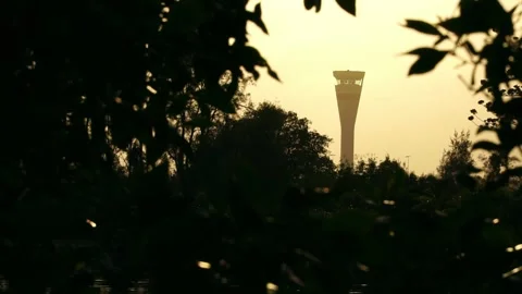 Backlit silhouette of Air Traffic Control tower, green trees in foreground Stock Footage 145559509