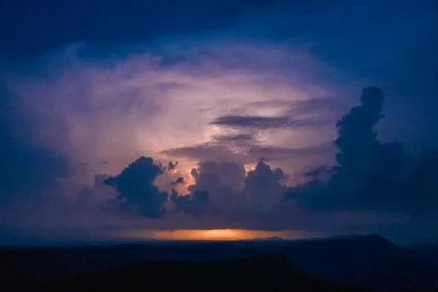 Backlit storm clouds above distant hills at night Stock Photos